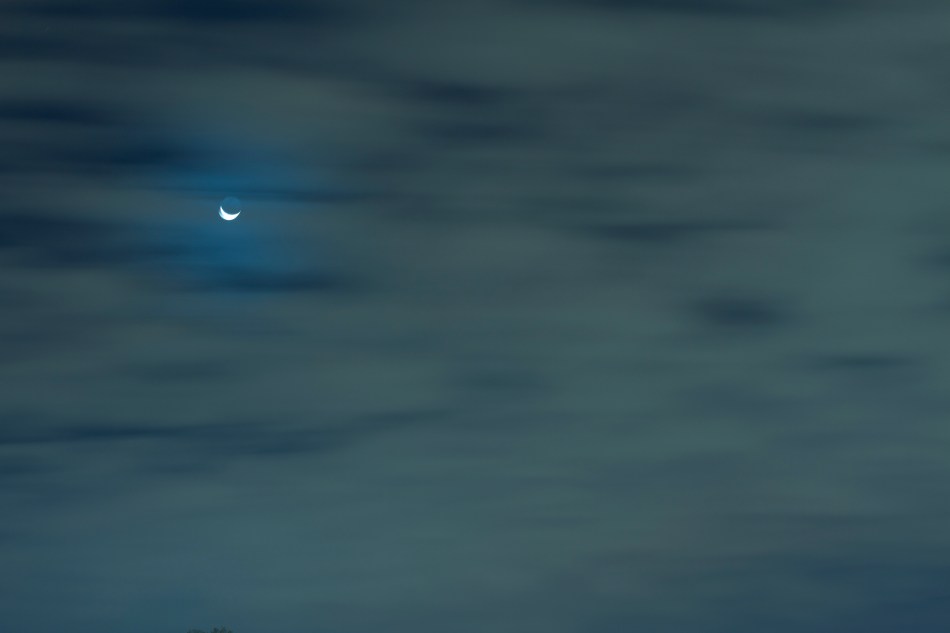 Crescent Moon in the night sky behind clouds