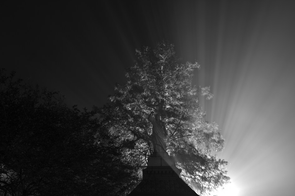 Rays of light emanating from behind a statue during a foggy night in New Orleans