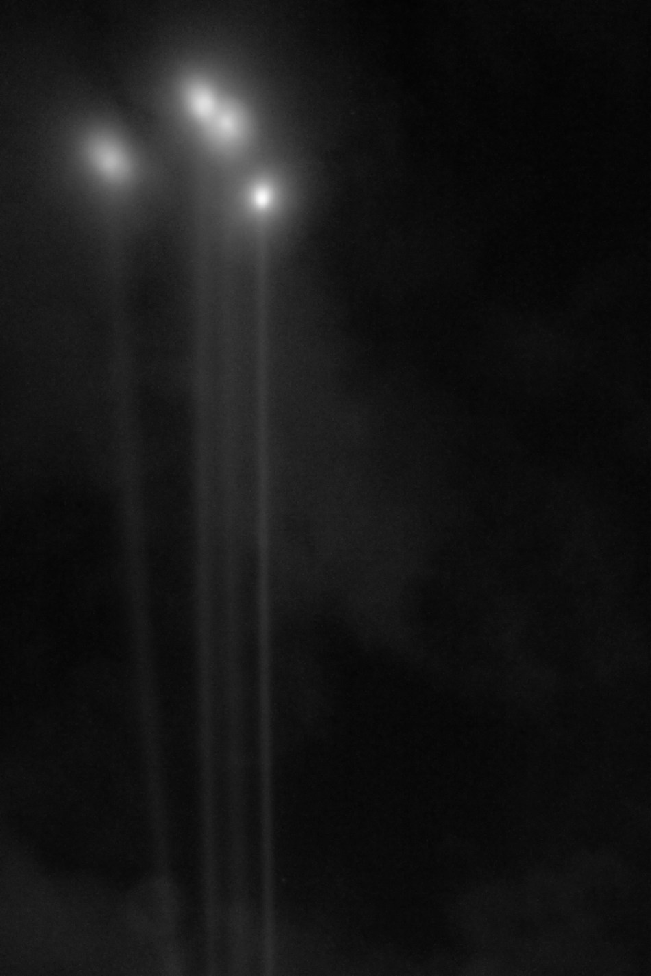 Four spotlights nearly converge in the night sky